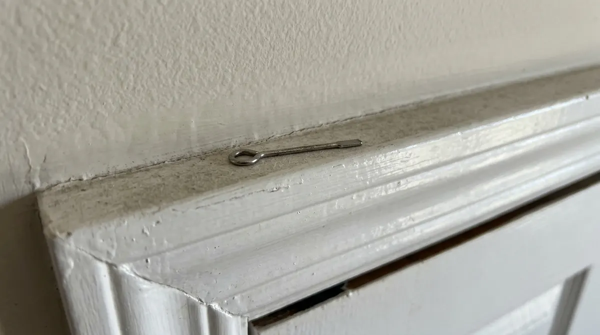 Small metal emergency door key tool resting on top of a door frame