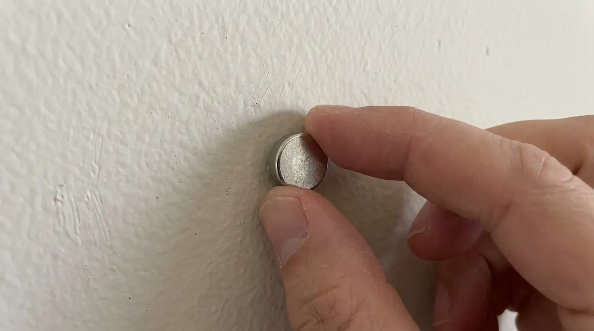 Small strong magnet stuck to a painted wall where a hidden drywall screw is